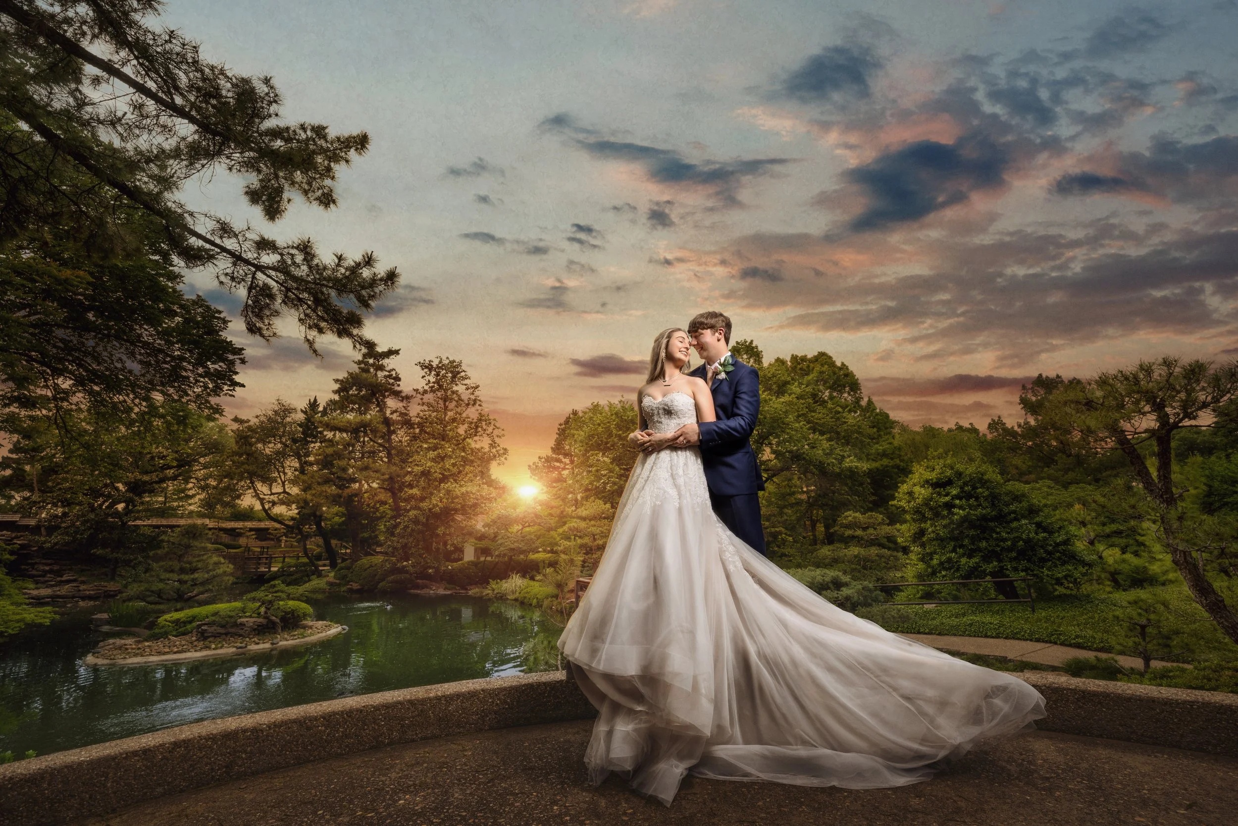 Bride and groom photographed outdoors at sunset with dramatic sky and garden landscape