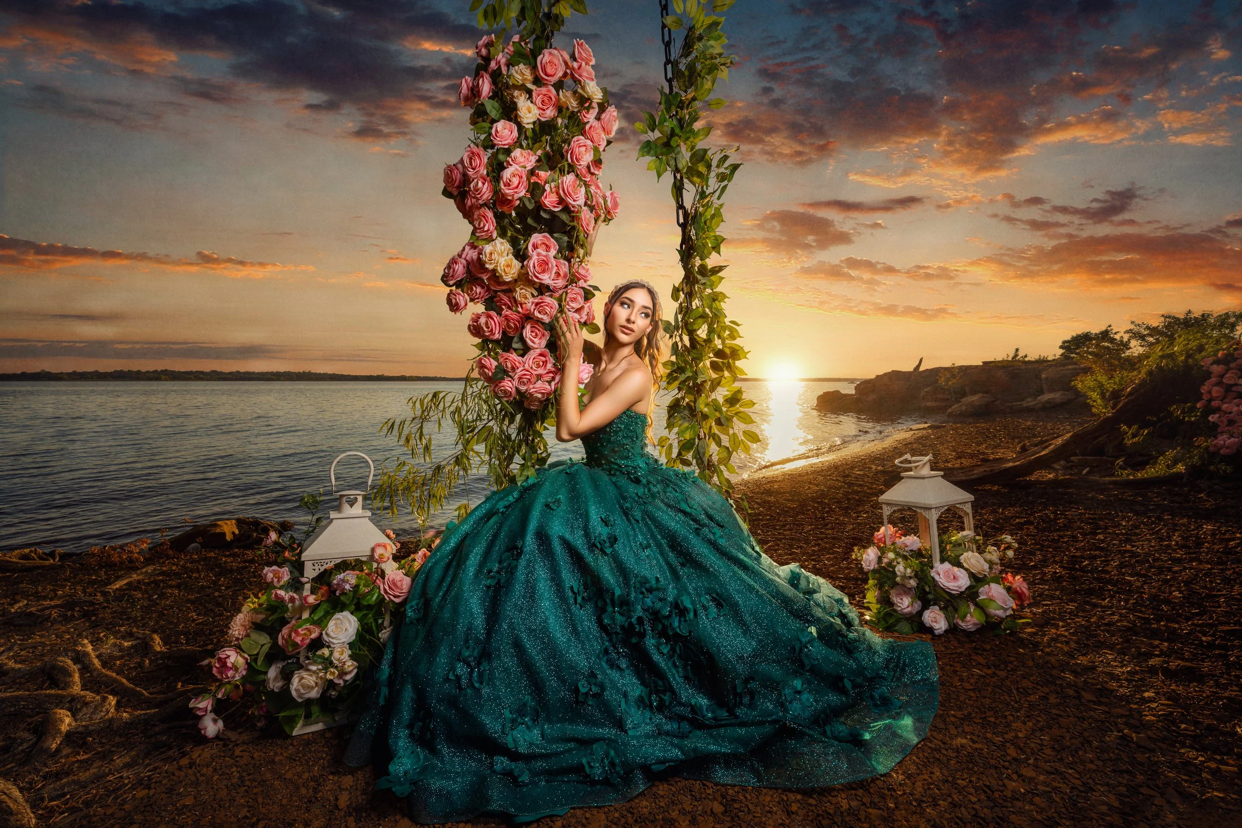 Quinceañera wearing an emerald green ball gown beside a floral swing during a cinematic sunset portrait session by the water.