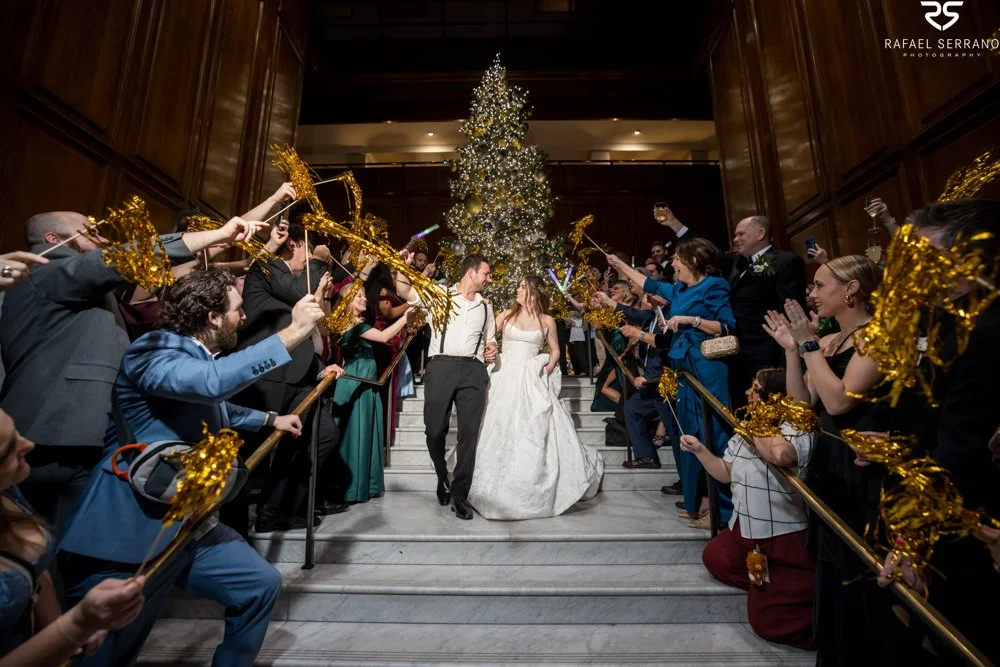 McKenna and Chris descending the hotel staircase as guests wave gold pom-poms.