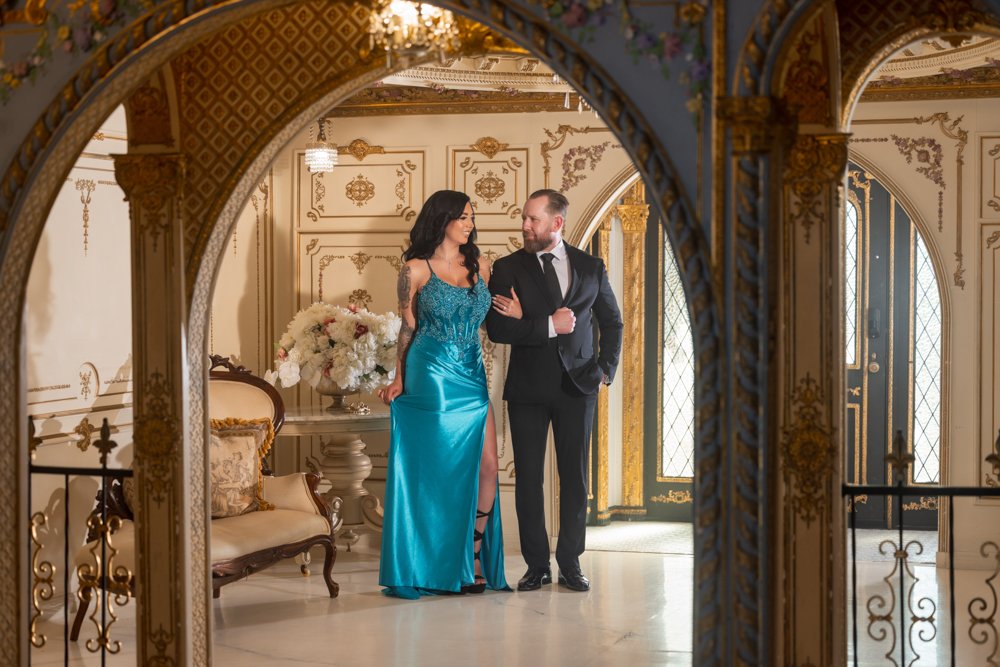 Couple looking toward each other beneath decorated arches, wearing a turquoise dress and dark suit.