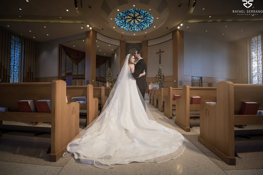 McKenna and Chris embracing in the church aisle with her dress and veil extending toward the camera.