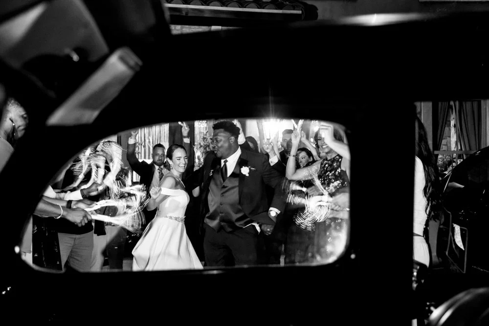 Black-and-white reflection of Mallory and Marcus in a vehicle mirror.