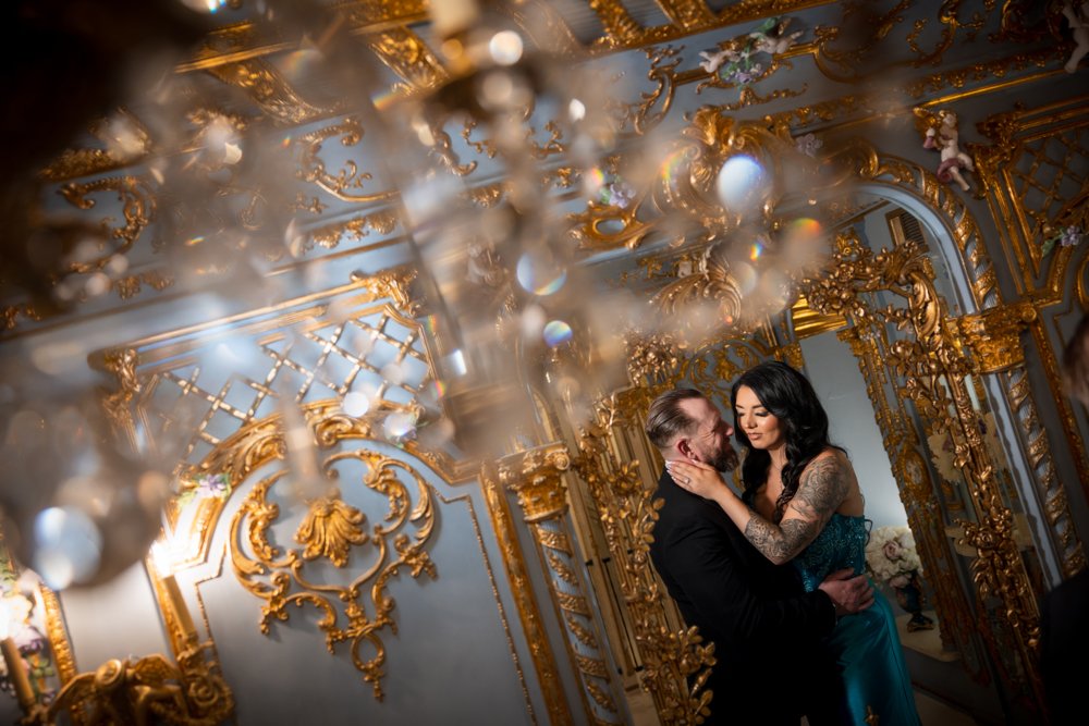 Couple standing together with softly blurred chandelier details in the foreground.