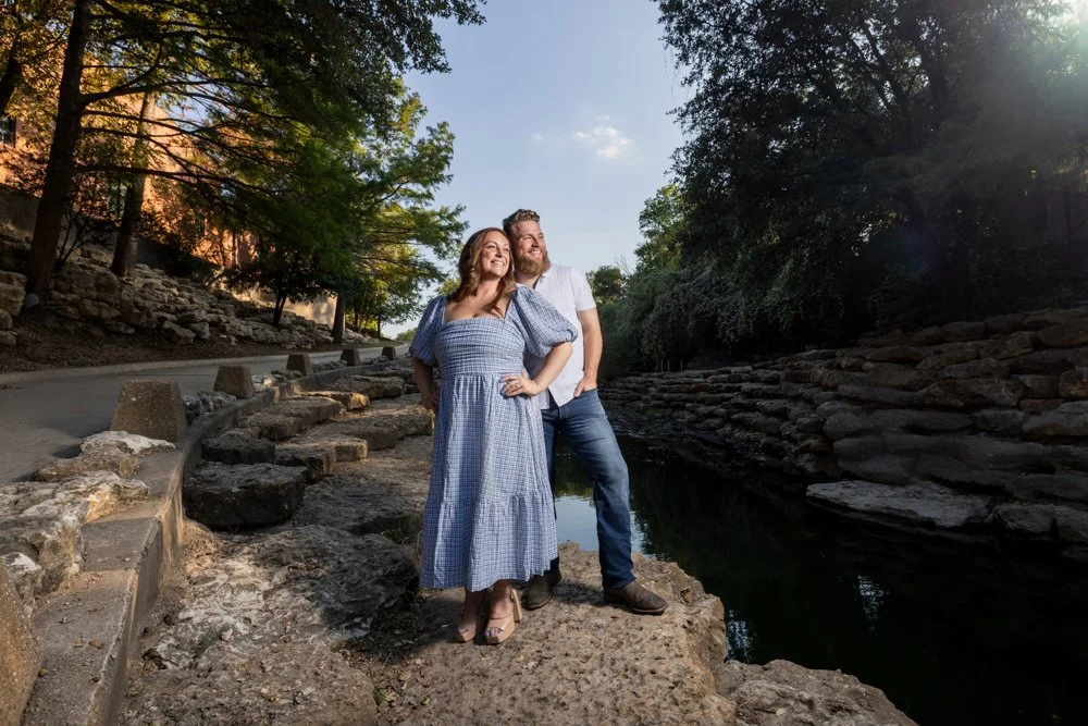 Lacey and Trey standing together beside water, rocks, and trees.