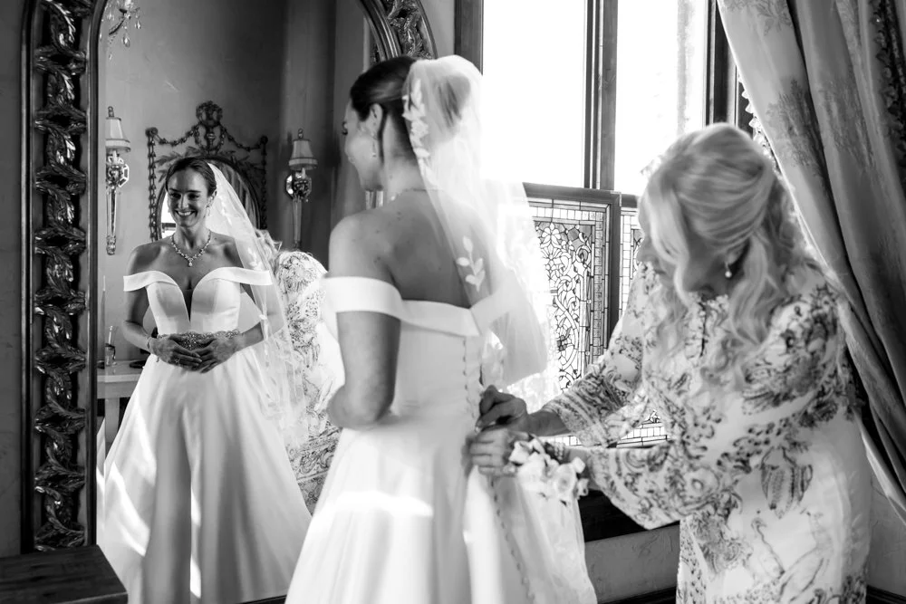 Black-and-white photograph of Mallory at a mirror during bridal preparations.