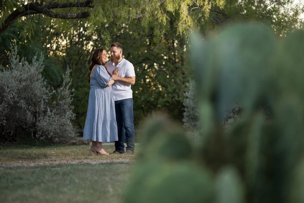 Lacey and Trey standing in greenery with a large blurred cactus in the foreground.