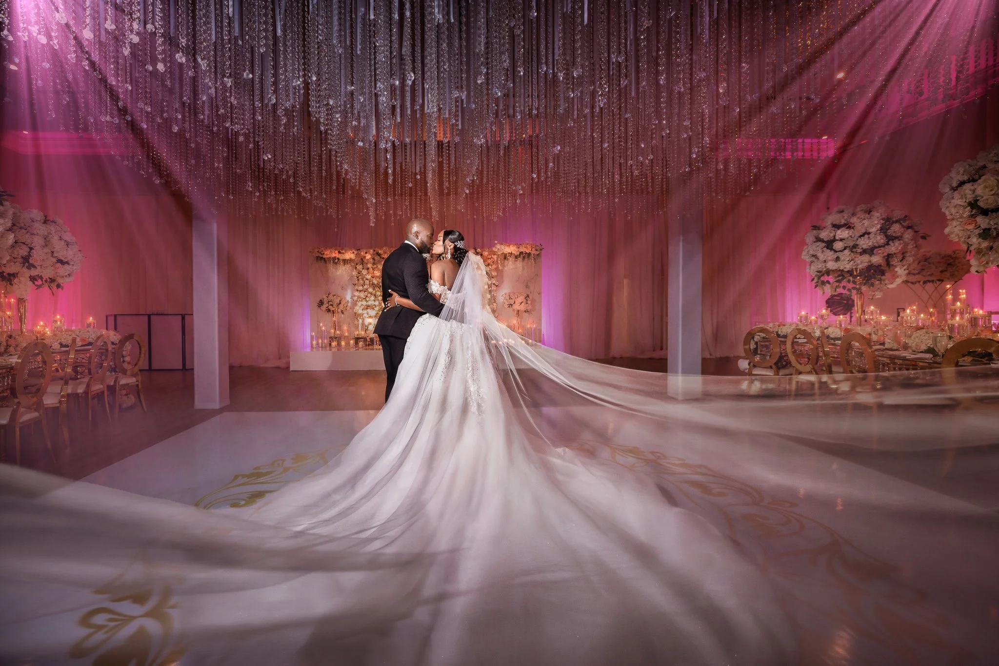 Bride and groom photographed during their wedding reception beneath dramatic hanging lights.