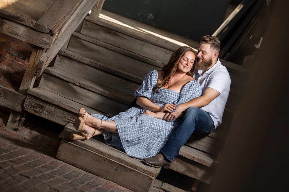 Lacey and Trey seated together against weathered wood in a tilted composition.