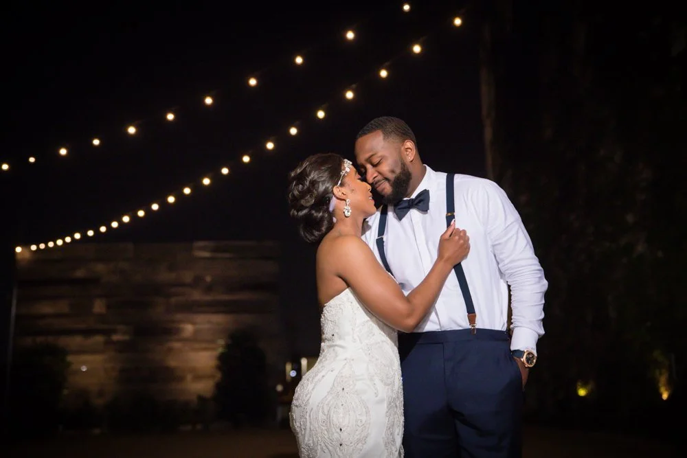 Bride and groom sharing an evening wedding portrait beneath string lights at The Brik in Fort Worth, Texas.