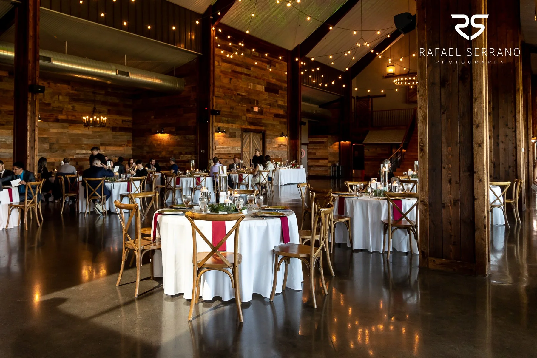 Wedding reception decorated inside a rustic venue with string lights, wood walls, and decorated tables.