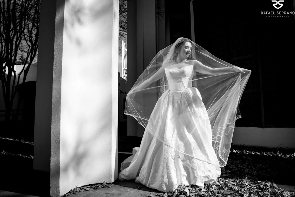 Black-and-white portrait of McKenna holding her veil open beside a white column.