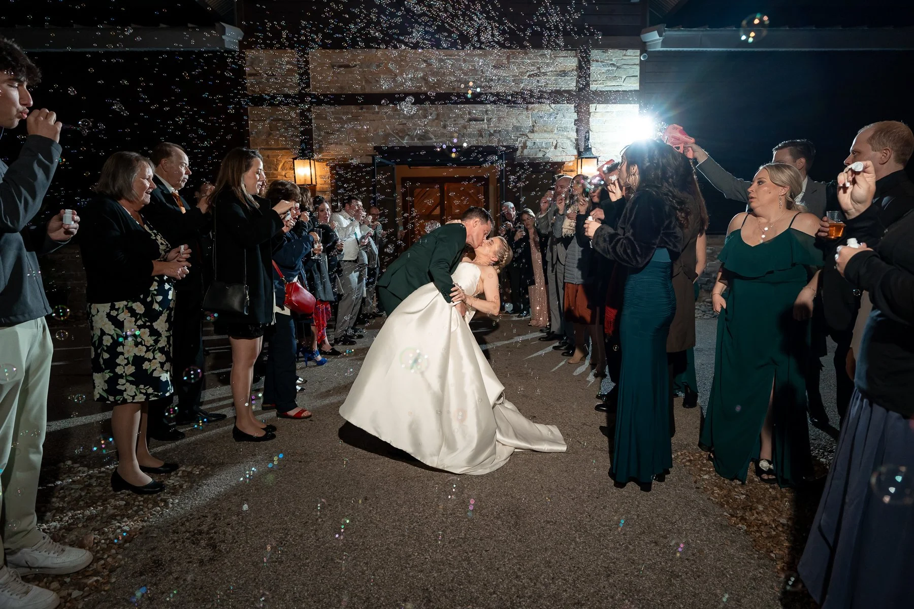 Bride and groom share a kiss surrounded by guests blowing bubbles at Stone Crest Venue in McKinney, TX.