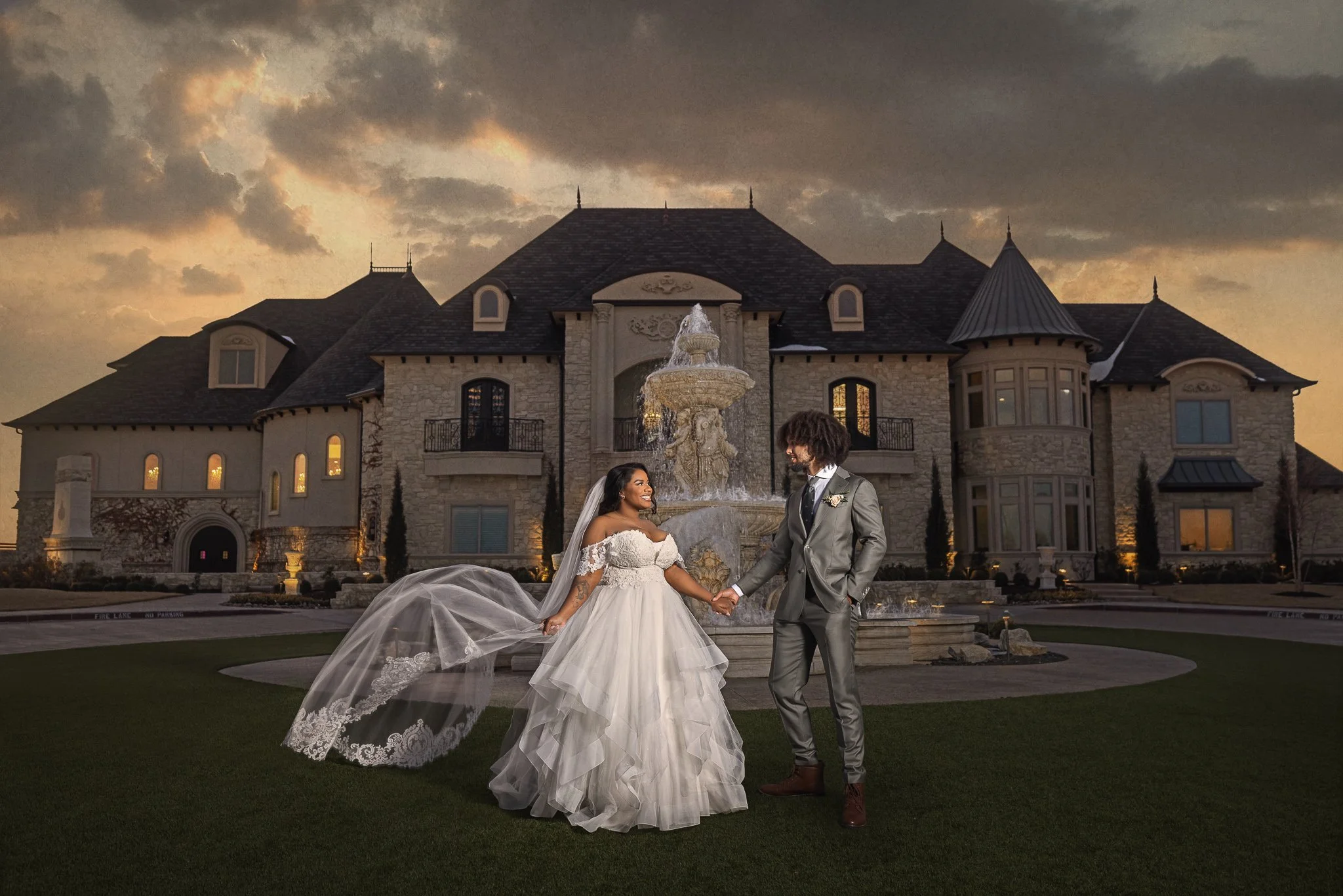 Bride and groom posing in front of an elegant wedding venue and fountain at sunset.