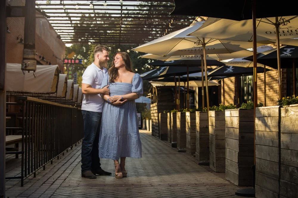 Lacey and Trey standing beneath an overhead structure beside patio umbrellas.