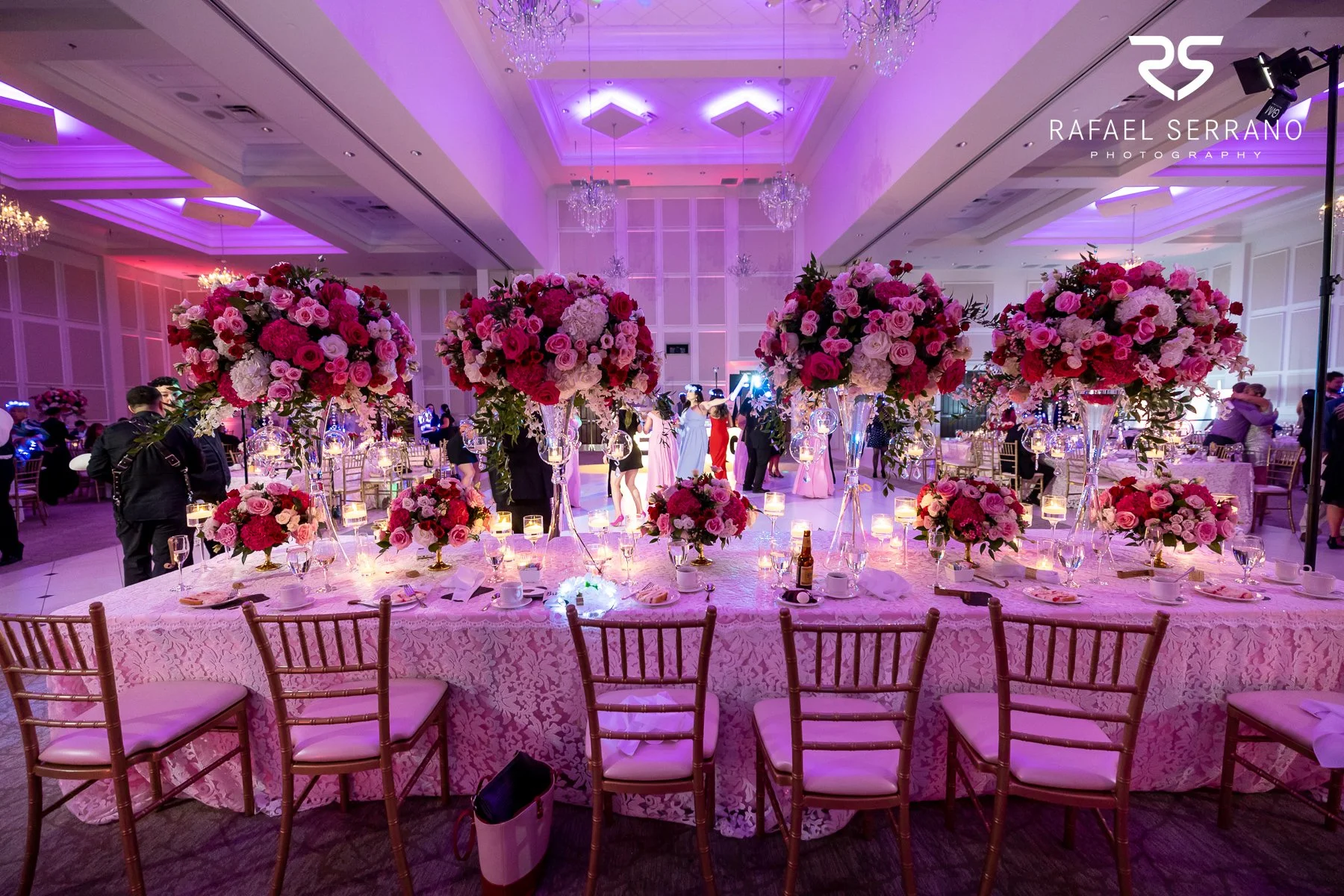 Wedding reception with floral centerpieces, candlelight, decorated tables, and purple ambient lighting.