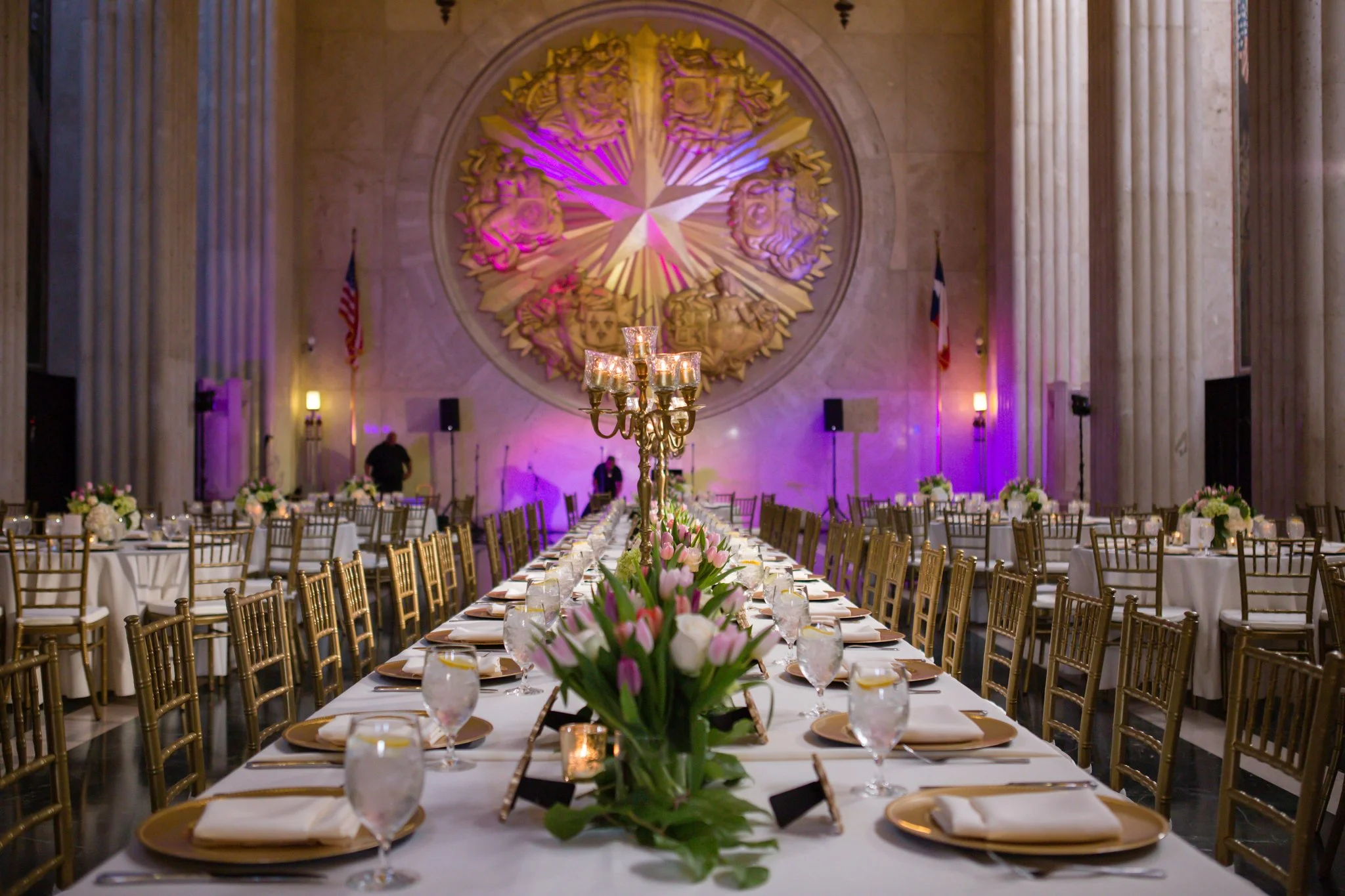 Wedding reception tables with floral centerpieces, gold place settings, candles, and coordinated decor.