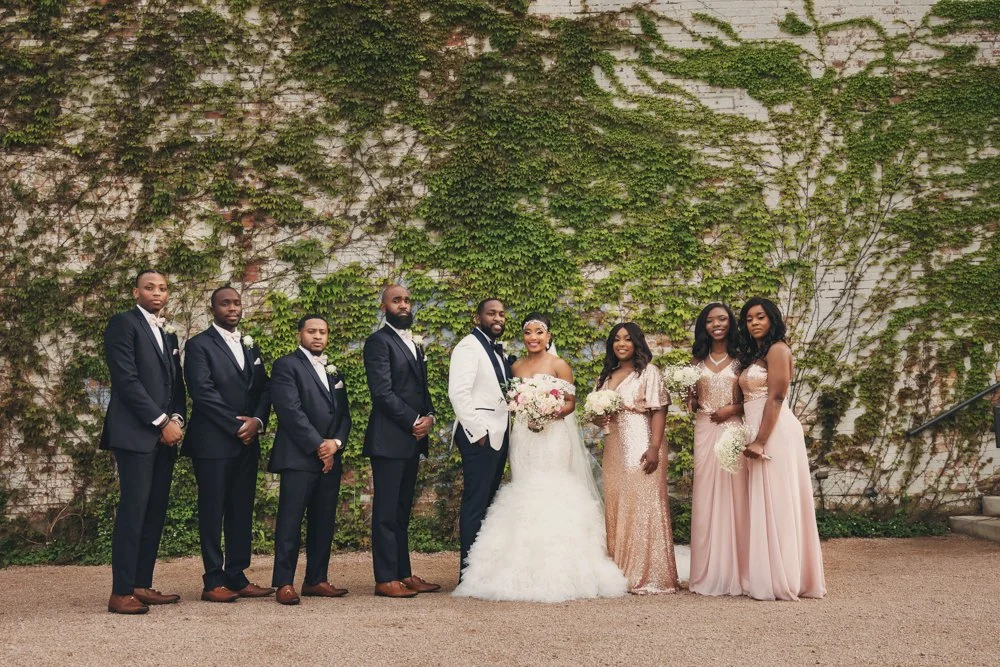 Bride, groom, bridesmaids, and groomsmen photographed against an ivy-covered wall at The Brik in Fort Worth, Texas.