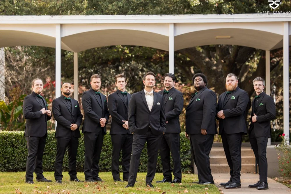 Chris and his wedding party in dark suits standing beneath an outdoor covered walkway.