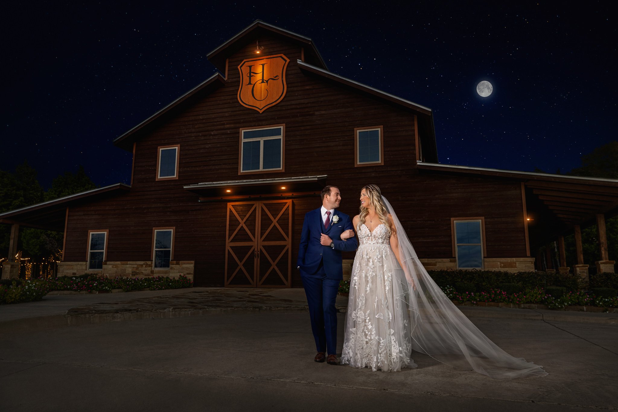 Bride and groom posing outside a wedding venue at night under a moonlit sky.