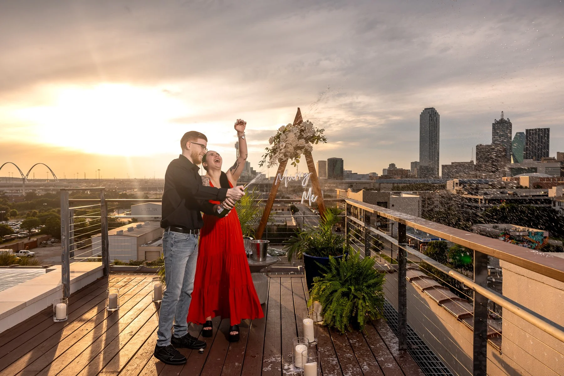 Newly engaged couple celebrating with champagne after a surprise proposal overlooking the Dallas skyline
