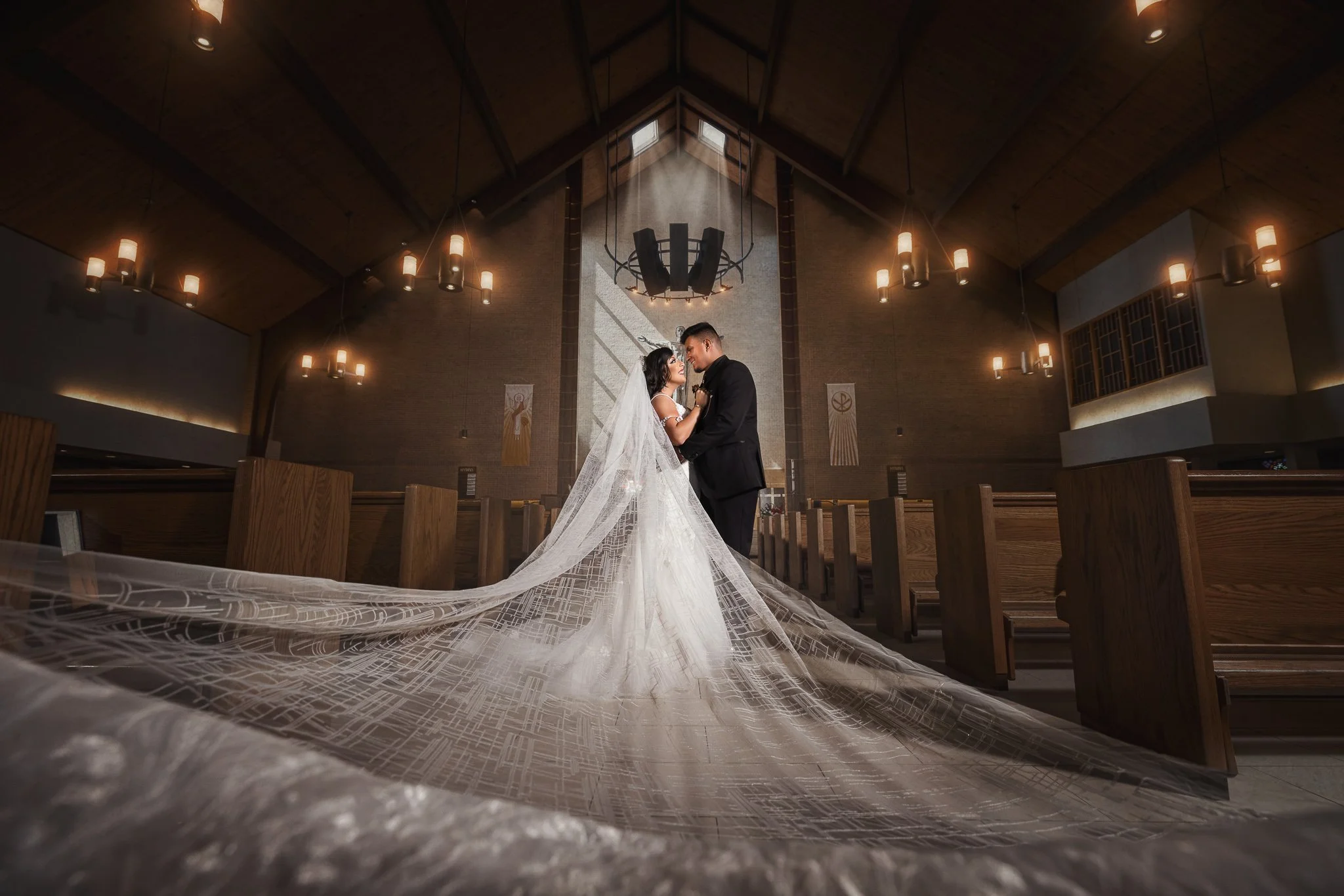 Bride and groom photographed inside a church with dramatic lighting and a long flowing veil.