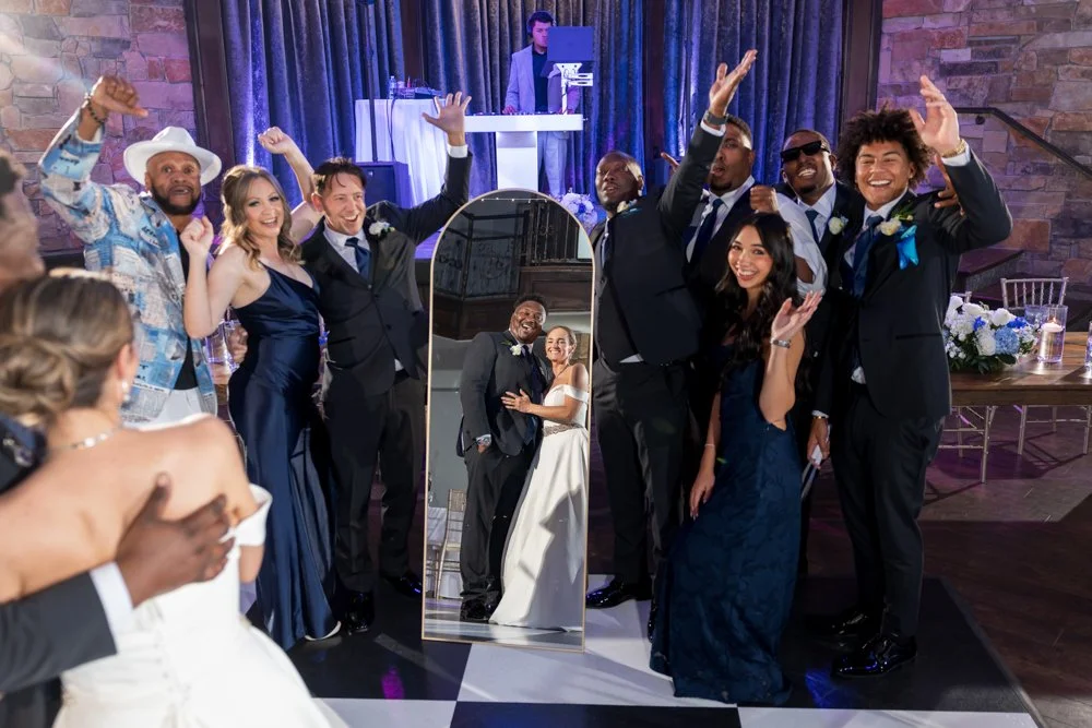 Wedding party gathered around a full-length mirror reflecting Mallory and Marcus.