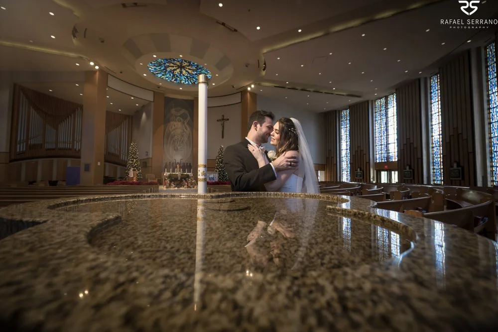 McKenna and Chris embracing inside the church with their reflection in a polished foreground surface.