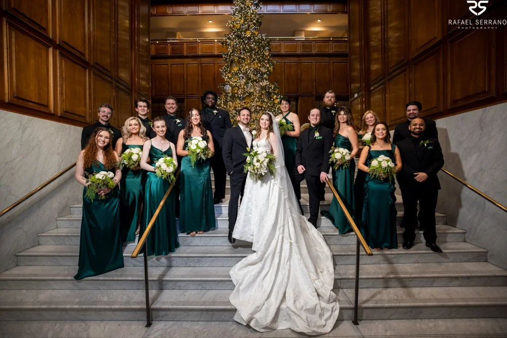 McKenna and Chris with their wedding party on The Adolphus staircase beneath a Christmas tree.