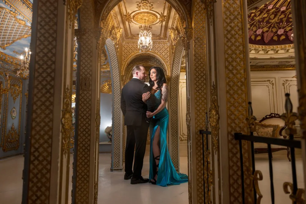 Couple embracing in a decorated passage beneath a chandelier.