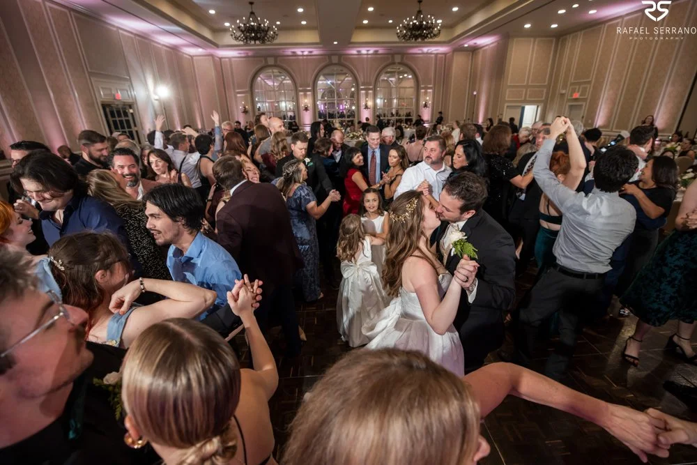 McKenna and Chris dancing together among guests on a full ballroom dance floor.