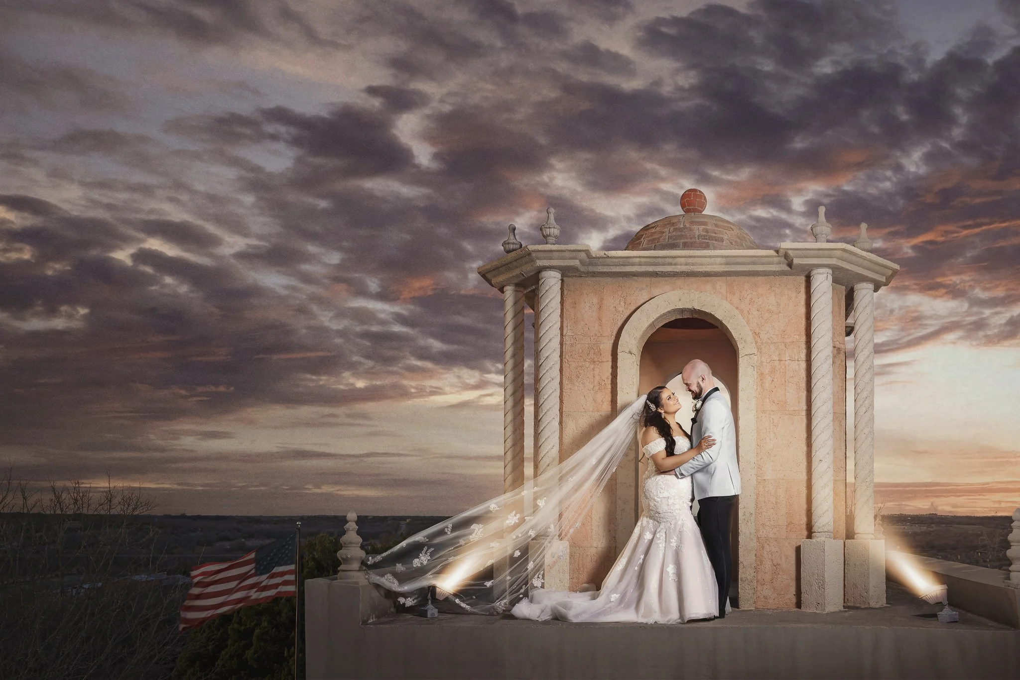 Bride and groom portrait at sunset beside an elegant outdoor structure with dramatic clouds.