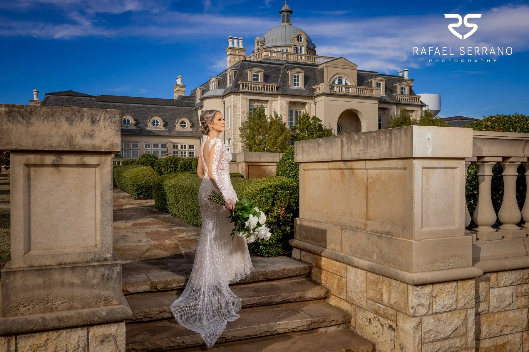 Bride wearing a fitted wedding dress while walking through an elegant outdoor venue.