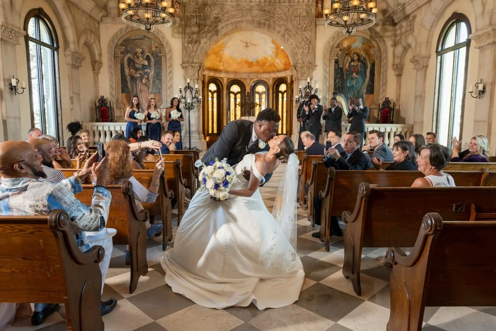 Marcus dipping and kissing Mallory in the chapel aisle as guests celebrate.