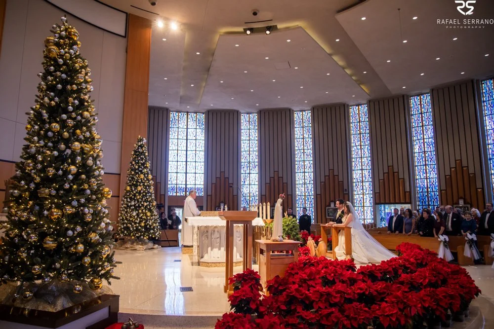 Wide view of McKenna and Chris’s ceremony at St. Monica with Christmas trees and red poinsettias.