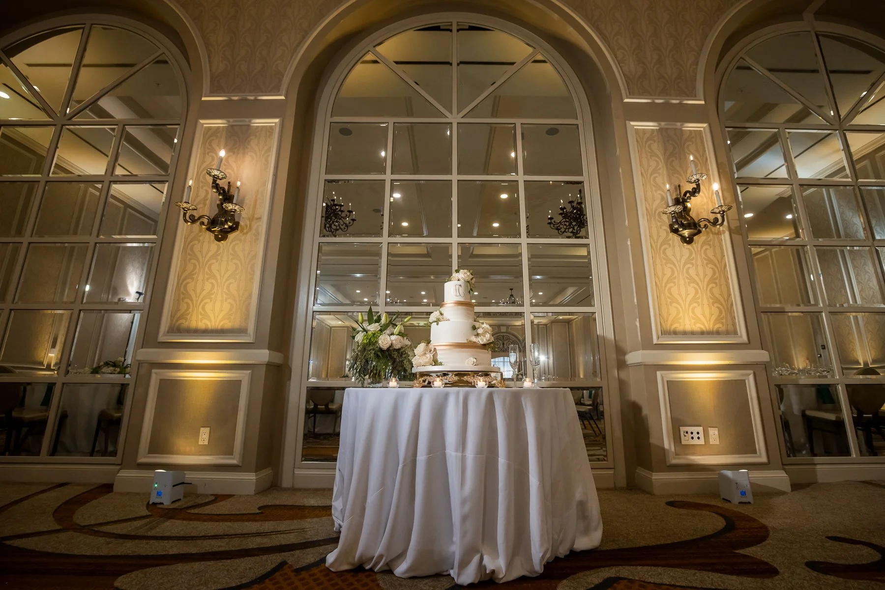Wedding cake displayed against the mirrored ballroom walls at The Adolphus Hotel