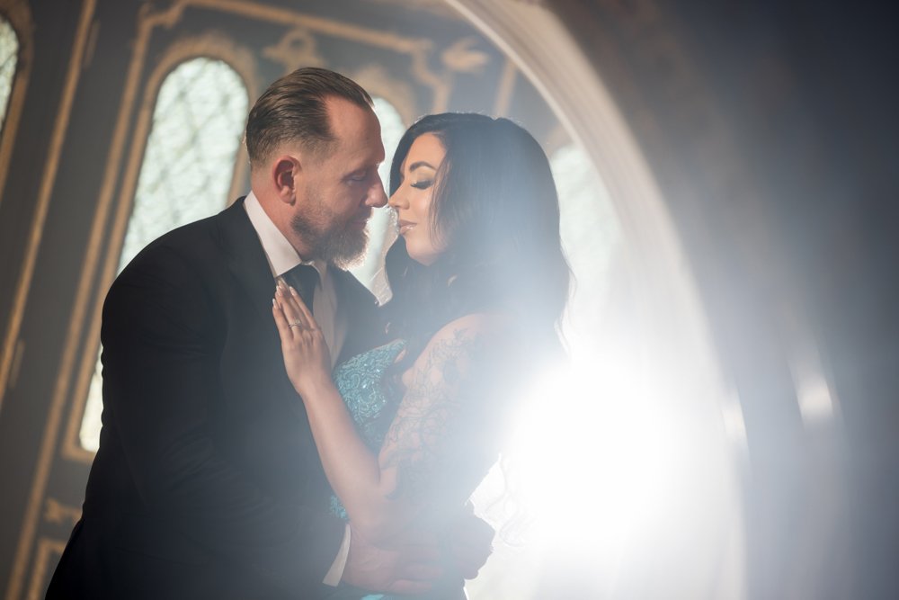 Couple leaning toward each other in a close portrait with bright light behind them.