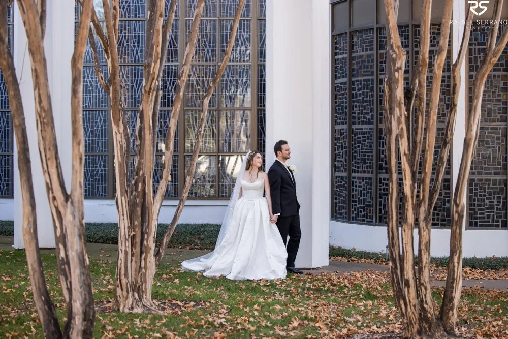 McKenna and Chris holding hands outside St. Monica, framed between trees and stained-glass windows.