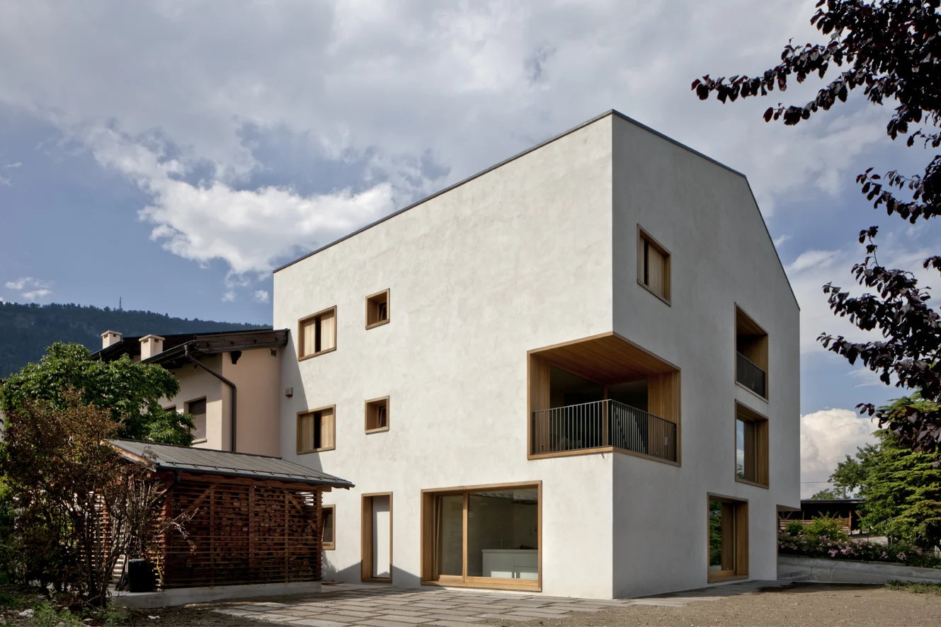 B&B Casa Incantata, Revò, Tn Tra i filari di mele della Val di Non, la demolizione e ricostruzione di un anonimo edificio residenziale degli anni '70 ha costituito l’occasione per recuperare il suo rapporto con il paesaggio e valorizzarne l’affaccio spettacolare sulla valle. La nuova architettura dal carattere formale estremamente semplificato, conserva proporzioni e volumetria originarie. Il linguaggio adottato reinterpreta i caratteri essenziali della tradizione alpina: corpo monolitico e compatto, intonaco bianco a finitura delle facciate, legno come naturale cornice delle aperture. Uniche eccezioni al vernacolo locale sono il contenimento della cornice di gronda all’interno delle murature perimetrali e la composizione libera delle aperture. I prospetti giocano, infatti, con la giustapposizione delle finestre, collocate in relazione ai diversi ambienti che sono chiamate a illuminare. La semplificazione dell’esterno dell’edificio si confronta con la ricchezza degli spazi interni, articolati attorno ad un monumentale vano scale. Collocato in posizione centrale, esso scandisce i diversi ambiti della casa attraverso rampe sovrapposte strette in un’intercapedine a doppia altezza. I tagli dei solai dilatano inaspettatamente lo spazio in senso verticale moltiplicando i traguardi visivi fra gli ambienti. Data: 2007 | 2011 Progettisti: Paolo De Benedictis, Glenda Flaim Progettista strutturale: Luca Pulignano Progettista impiantistico: Energytech G.m.b.H./S.r.l Fotografa: Alessandra Chemollo 2012 Premio di architettura città di Oderzo XIII edizione Progetto selezionato con menzione d’onore 2012 Selezione Nazionale RI.U.SO.01 2012. Rigenerazione Urbana Sostenibile Progetto Premiato 2013 Premio di architettura Costruire il Trentino 2009/2012 Progetto premiato ex aequo 2016 Rassegna Architetti Arco Alpino Casa Incantata - Progetto selezionato << cambia progetto >>