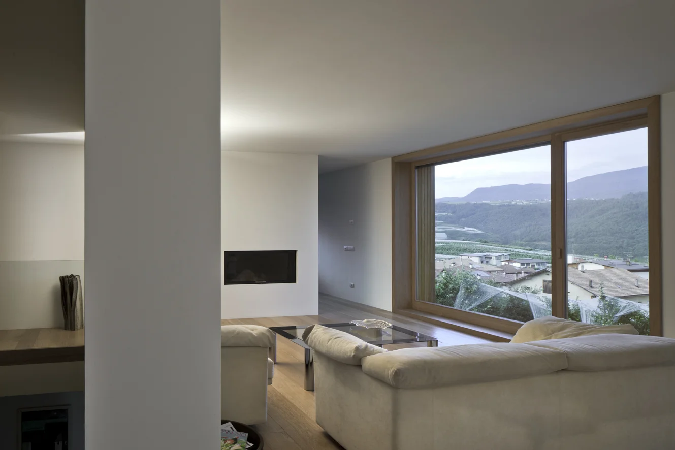 B&B Casa Incantata, Revò, Tn Tra i filari di mele della Val di Non, la demolizione e ricostruzione di un anonimo edificio residenziale degli anni '70 ha costituito l’occasione per recuperare il suo rapporto con il paesaggio e valorizzarne l’affaccio spettacolare sulla valle. La nuova architettura dal carattere formale estremamente semplificato, conserva proporzioni e volumetria originarie. Il linguaggio adottato reinterpreta i caratteri essenziali della tradizione alpina: corpo monolitico e compatto, intonaco bianco a finitura delle facciate, legno come naturale cornice delle aperture. Uniche eccezioni al vernacolo locale sono il contenimento della cornice di gronda all’interno delle murature perimetrali e la composizione libera delle aperture. I prospetti giocano, infatti, con la giustapposizione delle finestre, collocate in relazione ai diversi ambienti che sono chiamate a illuminare. La semplificazione dell’esterno dell’edificio si confronta con la ricchezza degli spazi interni, articolati attorno ad un monumentale vano scale. Collocato in posizione centrale, esso scandisce i diversi ambiti della casa attraverso rampe sovrapposte strette in un’intercapedine a doppia altezza. I tagli dei solai dilatano inaspettatamente lo spazio in senso verticale moltiplicando i traguardi visivi fra gli ambienti. Data: 2007 | 2011 Progettisti: Paolo De Benedictis, Glenda Flaim Progettista strutturale: Luca Pulignano Progettista impiantistico: Energytech G.m.b.H./S.r.l Fotografa: Alessandra Chemollo 2012 Premio di architettura città di Oderzo XIII edizione Progetto selezionato con menzione d’onore 2012 Selezione Nazionale RI.U.SO.01 2012. Rigenerazione Urbana Sostenibile Progetto Premiato 2013 Premio di architettura Costruire il Trentino 2009/2012 Progetto premiato ex aequo 2016 Rassegna Architetti Arco Alpino Casa Incantata - Progetto selezionato << cambia progetto >>