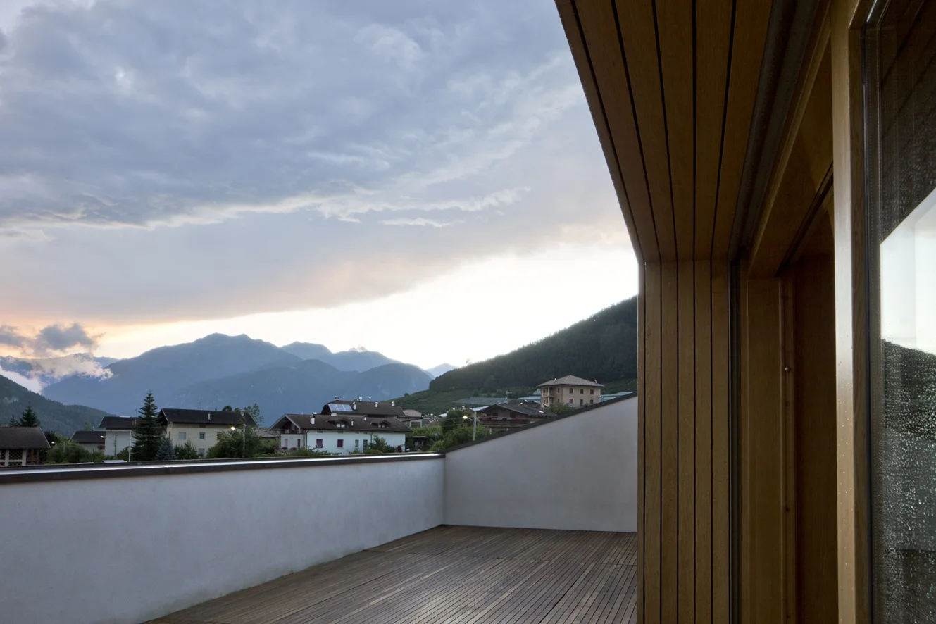 B&B Casa Incantata, Revò, Tn Tra i filari di mele della Val di Non, la demolizione e ricostruzione di un anonimo edificio residenziale degli anni '70 ha costituito l’occasione per recuperare il suo rapporto con il paesaggio e valorizzarne l’affaccio spettacolare sulla valle. La nuova architettura dal carattere formale estremamente semplificato, conserva proporzioni e volumetria originarie. Il linguaggio adottato reinterpreta i caratteri essenziali della tradizione alpina: corpo monolitico e compatto, intonaco bianco a finitura delle facciate, legno come naturale cornice delle aperture. Uniche eccezioni al vernacolo locale sono il contenimento della cornice di gronda all’interno delle murature perimetrali e la composizione libera delle aperture. I prospetti giocano, infatti, con la giustapposizione delle finestre, collocate in relazione ai diversi ambienti che sono chiamate a illuminare. La semplificazione dell’esterno dell’edificio si confronta con la ricchezza degli spazi interni, articolati attorno ad un monumentale vano scale. Collocato in posizione centrale, esso scandisce i diversi ambiti della casa attraverso rampe sovrapposte strette in un’intercapedine a doppia altezza. I tagli dei solai dilatano inaspettatamente lo spazio in senso verticale moltiplicando i traguardi visivi fra gli ambienti. Data: 2007 | 2011 Progettisti: Paolo De Benedictis, Glenda Flaim Progettista strutturale: Luca Pulignano Progettista impiantistico: Energytech G.m.b.H./S.r.l Fotografa: Alessandra Chemollo 2012 Premio di architettura città di Oderzo XIII edizione Progetto selezionato con menzione d’onore 2012 Selezione Nazionale RI.U.SO.01 2012. Rigenerazione Urbana Sostenibile Progetto Premiato 2013 Premio di architettura Costruire il Trentino 2009/2012 Progetto premiato ex aequo 2016 Rassegna Architetti Arco Alpino Casa Incantata - Progetto selezionato << cambia progetto >>