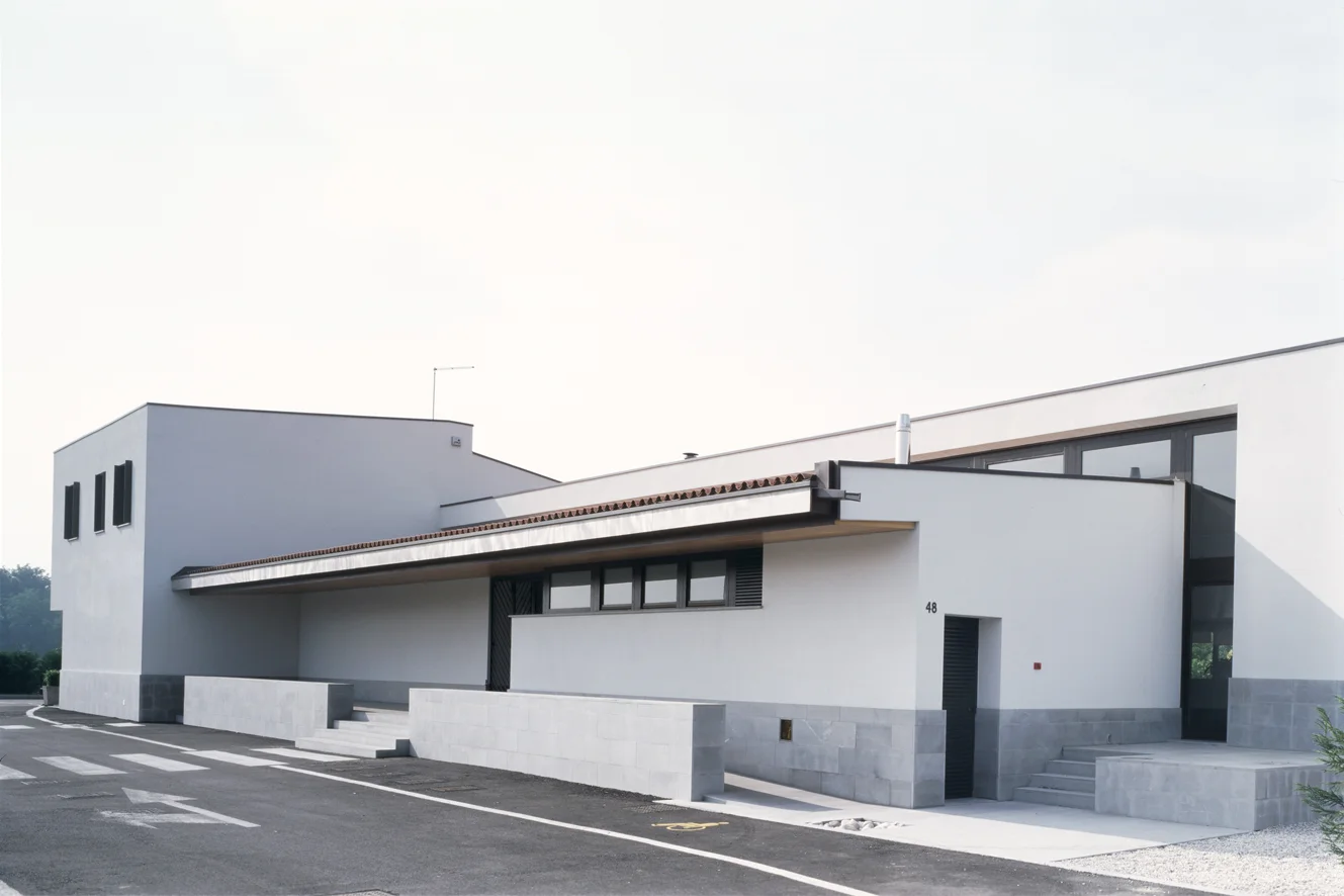 Ristorante Al Fogher, Camponogara, Ve L’edificio si trova su un’area rurale alla periferia di un piccolo centro vicino alla Riviera del Brenta, nei pressi di Dolo. Il progetto instaura con la campagna circostante un rapporto visivo e di dialogo attraverso il recupero e la reinterpretazione di elementi della tradizione: grandi logge finestrate, portici, tetti a falde. Due volumi di differente altezza, si addossano ad un terzo più alto posto sul retro. I due corpi in prossimità della strada, contengono, l’uno l’ingresso ed i servizi, l’altro la sala ristorante aperta a sud verso la campagna; il corpo sul fondo contiene le cucine e l’appartamento dei proprietari. La chiara organizzazione dei volumi si ritrova anche nell’organizzazione degli spazi interni. Data: 2000 | 2005 Progettisti: Paolo De Benedictis, Enrico Maria Raschi Progettista strutturale: Luca Pulignano Progettista impiantistico: Studio Vio Fotografa: Alessandra Chemollo << cambia progetto >>