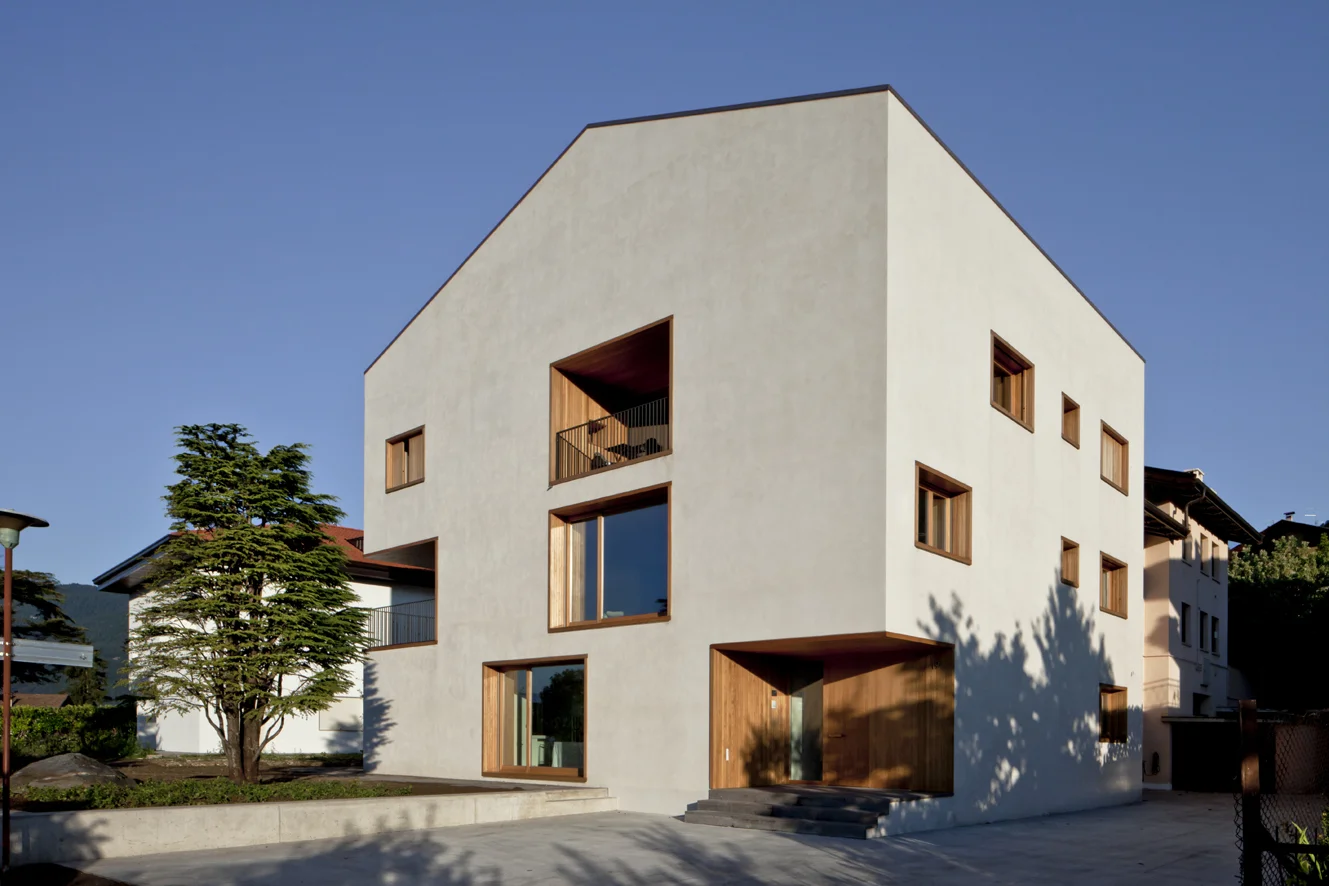 B&B Casa Incantata, Revò, Tn Amongst the rows of apple trees in the Val di Non, the demolition and reconstruction of an anonymous 1970s residential building provided the opportunity to retrieve the building’s relationship with the landscape and value the spectacular view over the valley. The new, formal and extremely simplified architecture retains the original proportions and volumes. The project reinterprets the essential features of the alpine architectural tradition: monolithic and compact body, white plaster on the façades, and wood as natural frame for windows Exceptions to this local style are the embedding of the eaves within the perimeter walls and the free composition of the openings. The façades play with the juxtaposition of the windows, which are placed in relation to the different spaces that they are meant to light up. The simplification of the exterior of the building contrasts with the interior spatial complexity that is articulated around a monumental stairwell. Centrally located, the latter divides the various areas of the house through overlapping flights of stairs that are cast in a two-level gap between the walls. The cuts through the floor slabs unexpectedly open up the space vertically and multiplying the visual links between the rooms. Date: 2007 | 2011 Architects: Paolo De Benedictis, Glenda Flaim Structural Engineer: Luca Pulignano Services Engineer: Energytech G.m.b.H./S.r.l Photography: Alessandra Chemollo 2012 Oderzo City Architecture Prize XIII edition Selected Project with honorable mention 2012 National Selection RI.U.SO.01 2012. Sustainable Urban Rigeneration First prize-winning project 2013 Building Trentino Architecture Prize 2009/2012 Ex aequo prize-winning project 2016 Prize Architetti Arco Alpino Selected project << change project >>