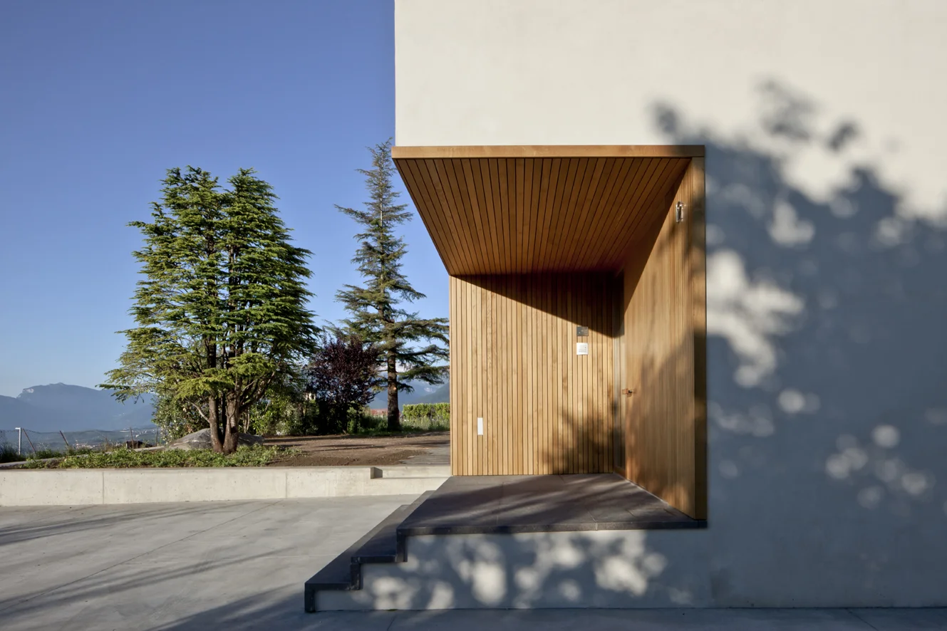B&B Casa Incantata, Revò, Tn Amongst the rows of apple trees in the Val di Non, the demolition and reconstruction of an anonymous 1970s residential building provided the opportunity to retrieve the building’s relationship with the landscape and value the spectacular view over the valley. The new, formal and extremely simplified architecture retains the original proportions and volumes. The project reinterprets the essential features of the alpine architectural tradition: monolithic and compact body, white plaster on the façades, and wood as natural frame for windows Exceptions to this local style are the embedding of the eaves within the perimeter walls and the free composition of the openings. The façades play with the juxtaposition of the windows, which are placed in relation to the different spaces that they are meant to light up. The simplification of the exterior of the building contrasts with the interior spatial complexity that is articulated around a monumental stairwell. Centrally located, the latter divides the various areas of the house through overlapping flights of stairs that are cast in a two-level gap between the walls. The cuts through the floor slabs unexpectedly open up the space vertically and multiplying the visual links between the rooms. Date: 2007 | 2011 Architects: Paolo De Benedictis, Glenda Flaim Structural Engineer: Luca Pulignano Services Engineer: Energytech G.m.b.H./S.r.l Photography: Alessandra Chemollo 2012 Oderzo City Architecture Prize XIII edition Selected Project with honorable mention 2012 National Selection RI.U.SO.01 2012. Sustainable Urban Rigeneration First prize-winning project 2013 Building Trentino Architecture Prize 2009/2012 Ex aequo prize-winning project 2016 Prize Architetti Arco Alpino Selected project << change project >>