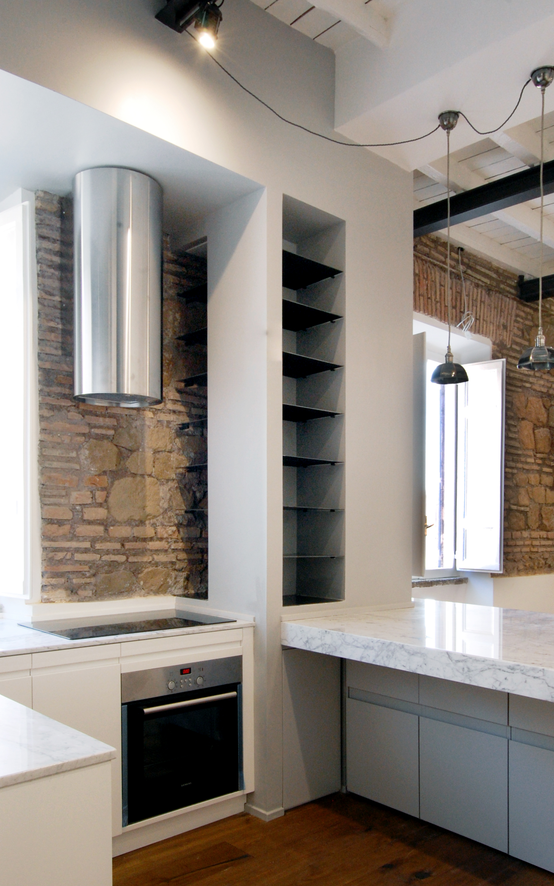 La cucina aperta sul living, con la zona cottura contenuta nello spessore del setto di servizio grigio e riparata alla vista dal piano in marmo.