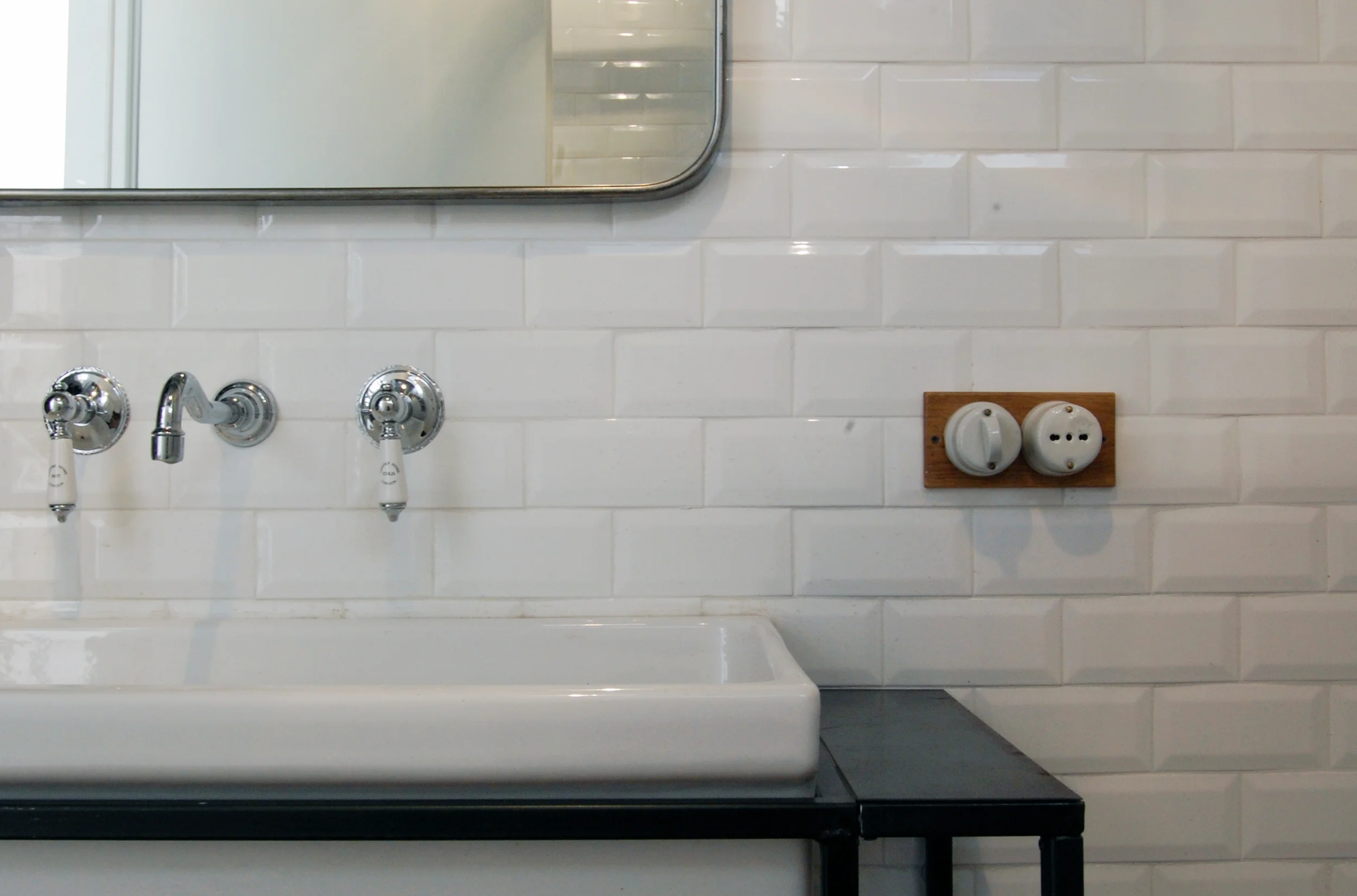 Un dettaglio del bagno, con il lavandino incassato in un struttura metallica e i pulsanti in ceramica su placca in legno.