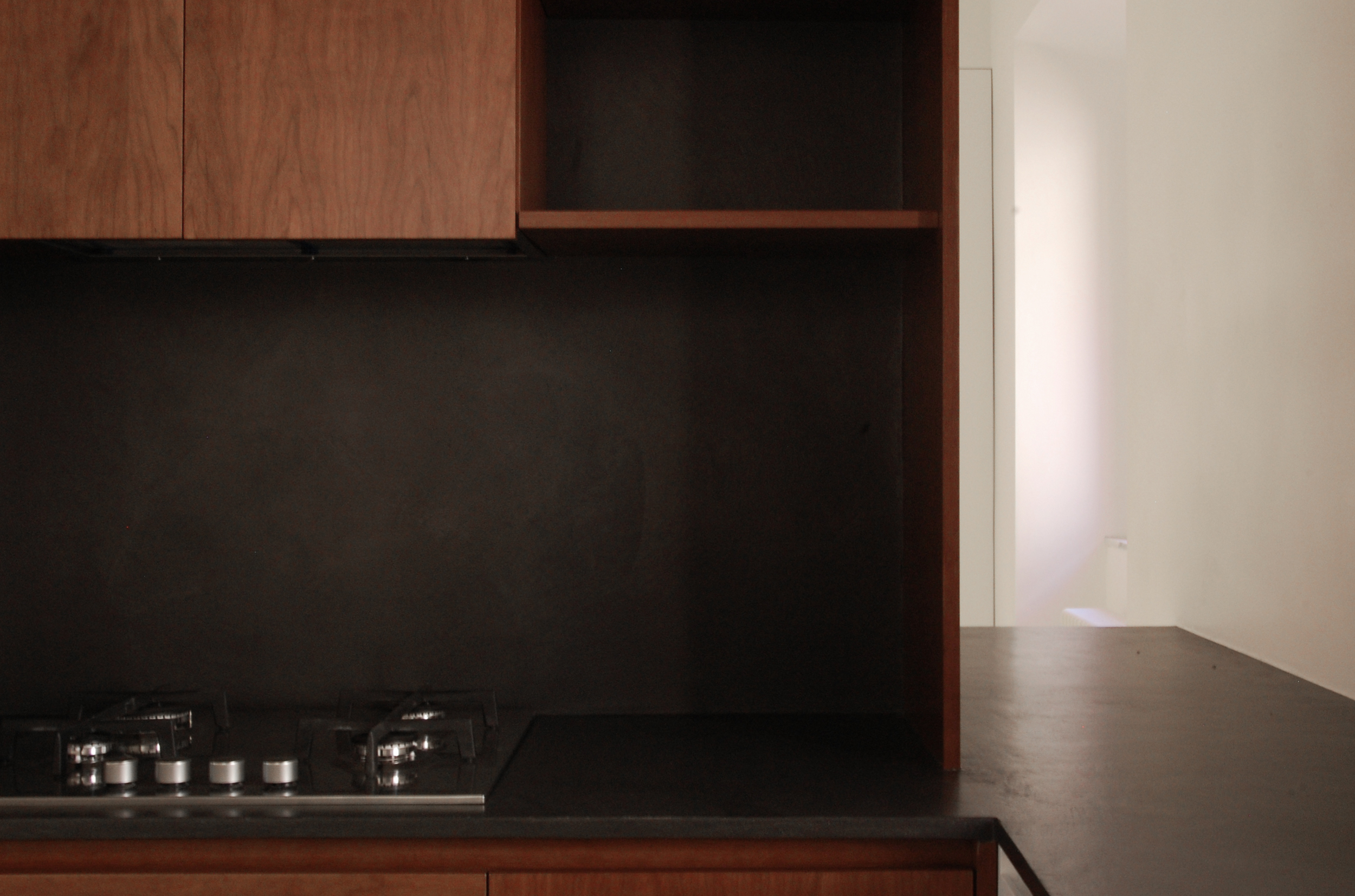Immagine di dettaglio: la parete attrezzata della cucina in primo piano, con la luce proveniente dalla zona living sullo sfondo.