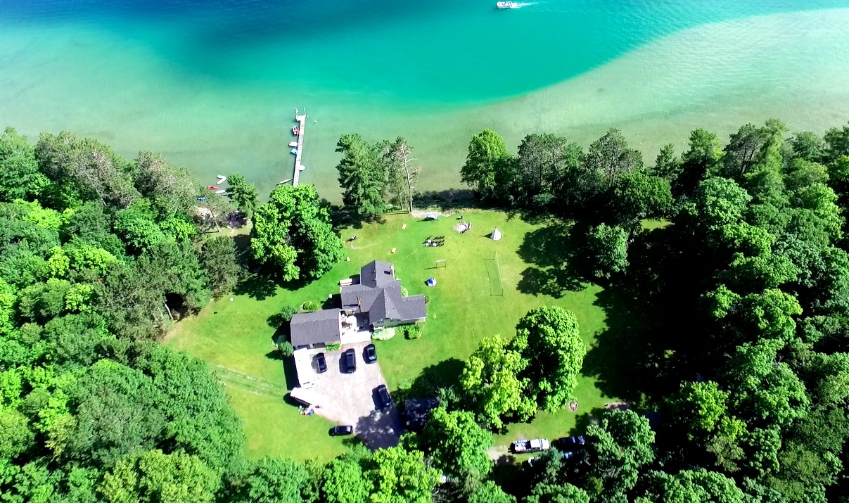 Just beyond the dock at Sugarcrest is a sandy shelf that sits over a steep, curving drop off. In the foreground is the main house along with two fire pits, volleyball court, wedding altar, an outdoor movie screen brought by guests and adirondack chair seating.