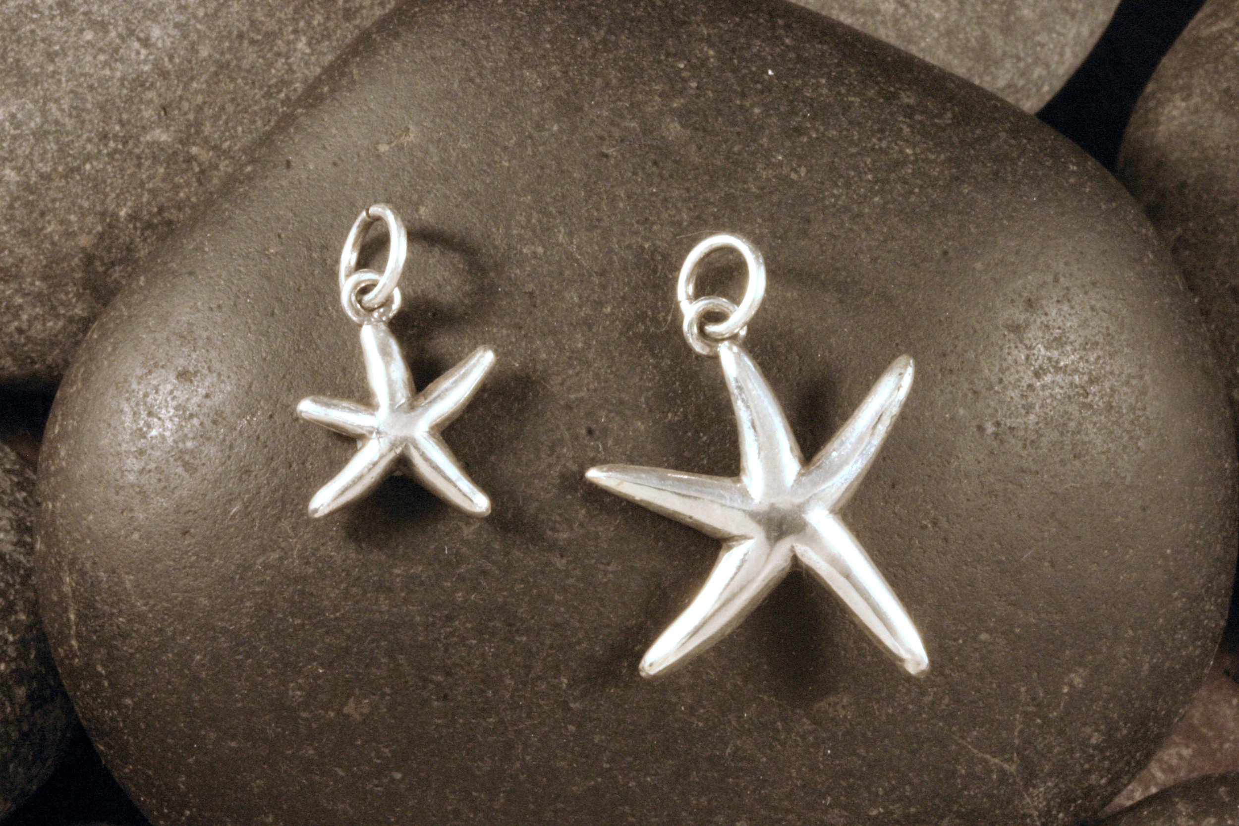 Small and medium sterling silver dancing starfish charms displayed on a rock.