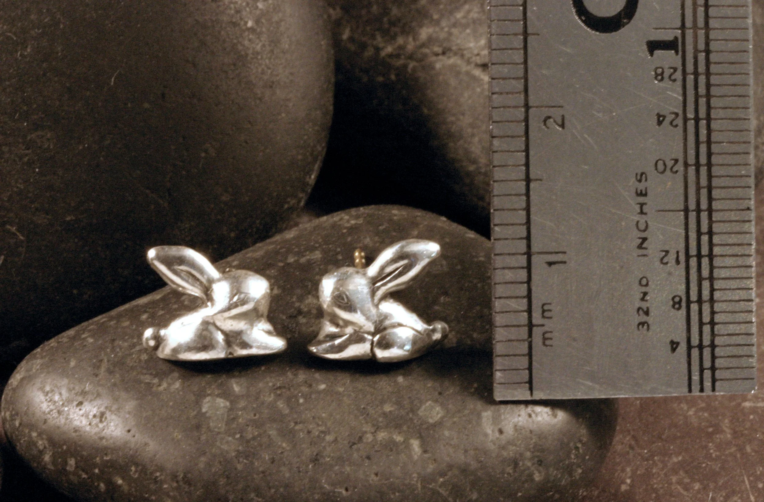 Sterling silver stylized rabbit studs next to a ruler.