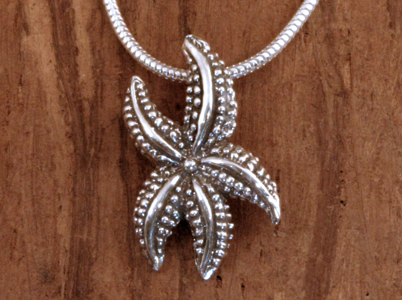 Oxidized sterling silver stylized dancing starfish pendant on craft paper.